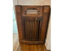 Vintage wooden console radio with polished cabinet, speaker grille, and control panel featuring dials and frequency display