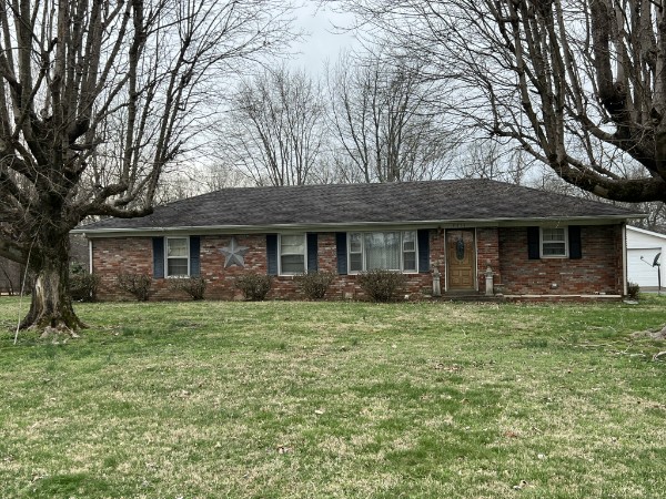 Residential real estate auction home — single‑story brick house with dark roof, decorative star on front wall, and leafless trees in yard