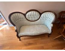 Antique upholstered loveseat with triple‑arched button‑tufted back and carved wooden frame